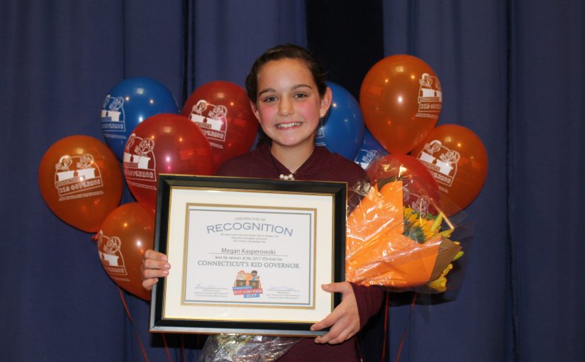 CTKG Megan stands with certificate of recognition in front of red, orange, and blue balloons.